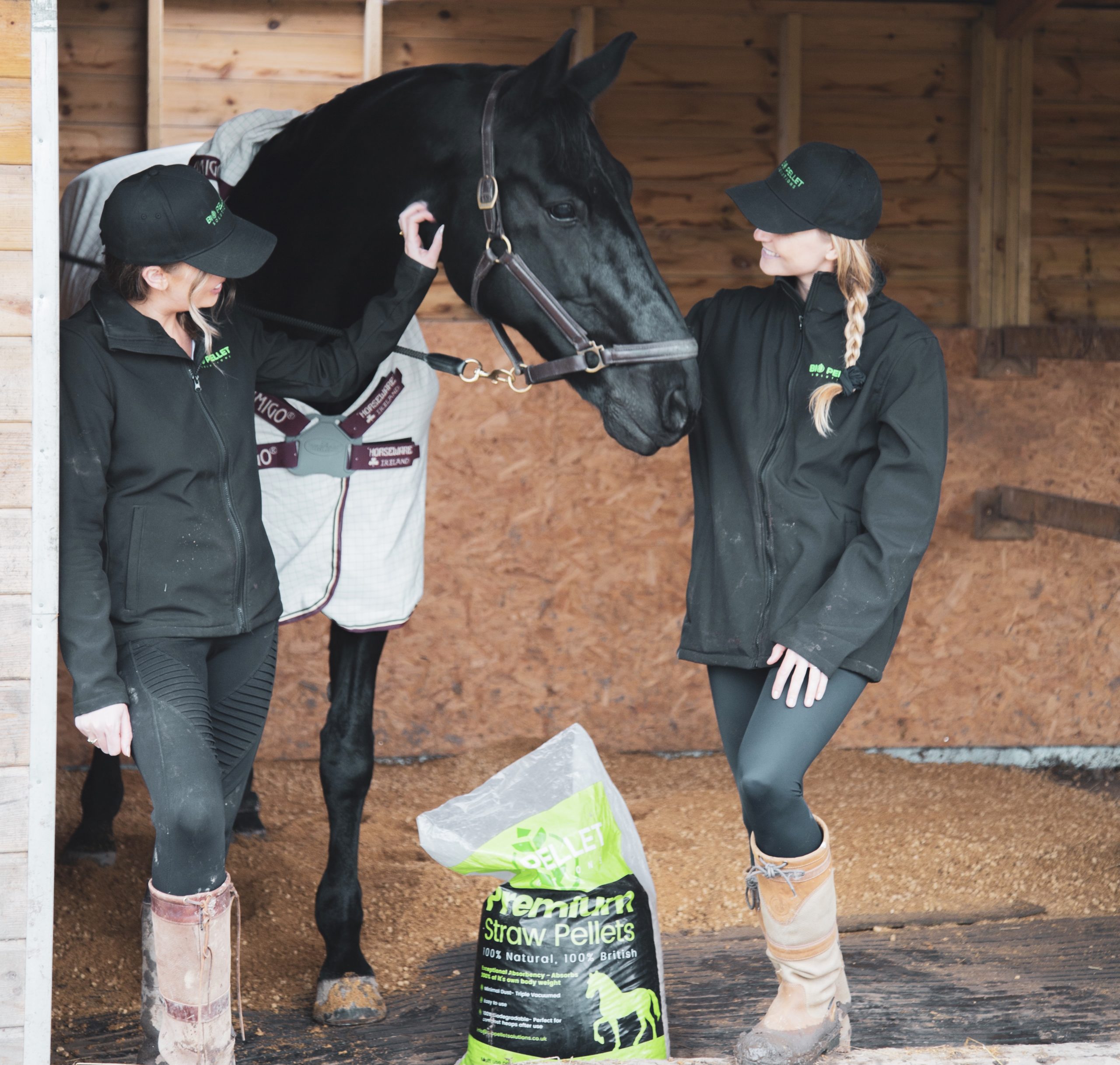 Two women stood either side of a black horse with a bag of Biopellets between them